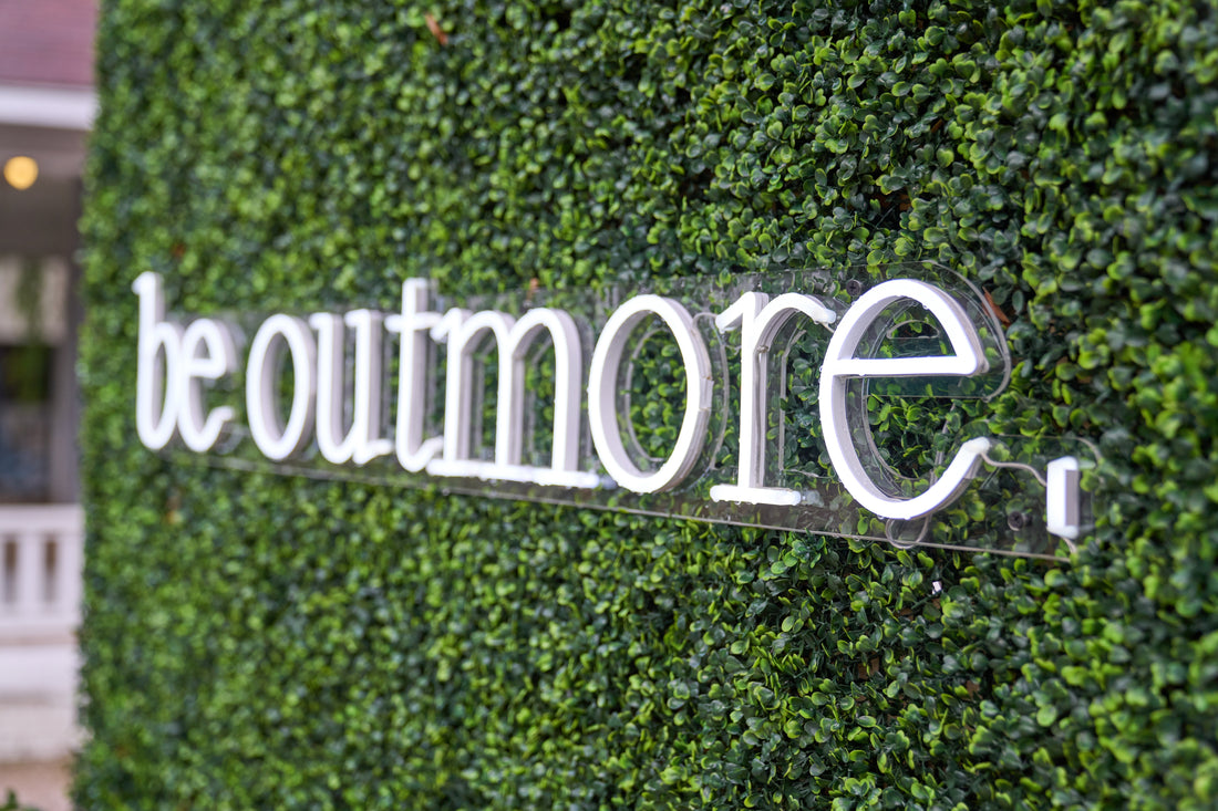 'be outmore' neon sign on green hedge wall